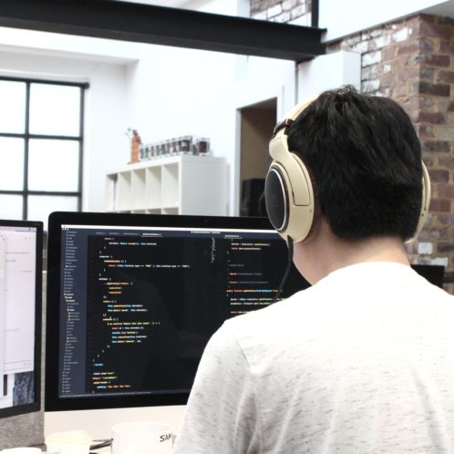 Man with headphones is working on his computer and is coding making websites.